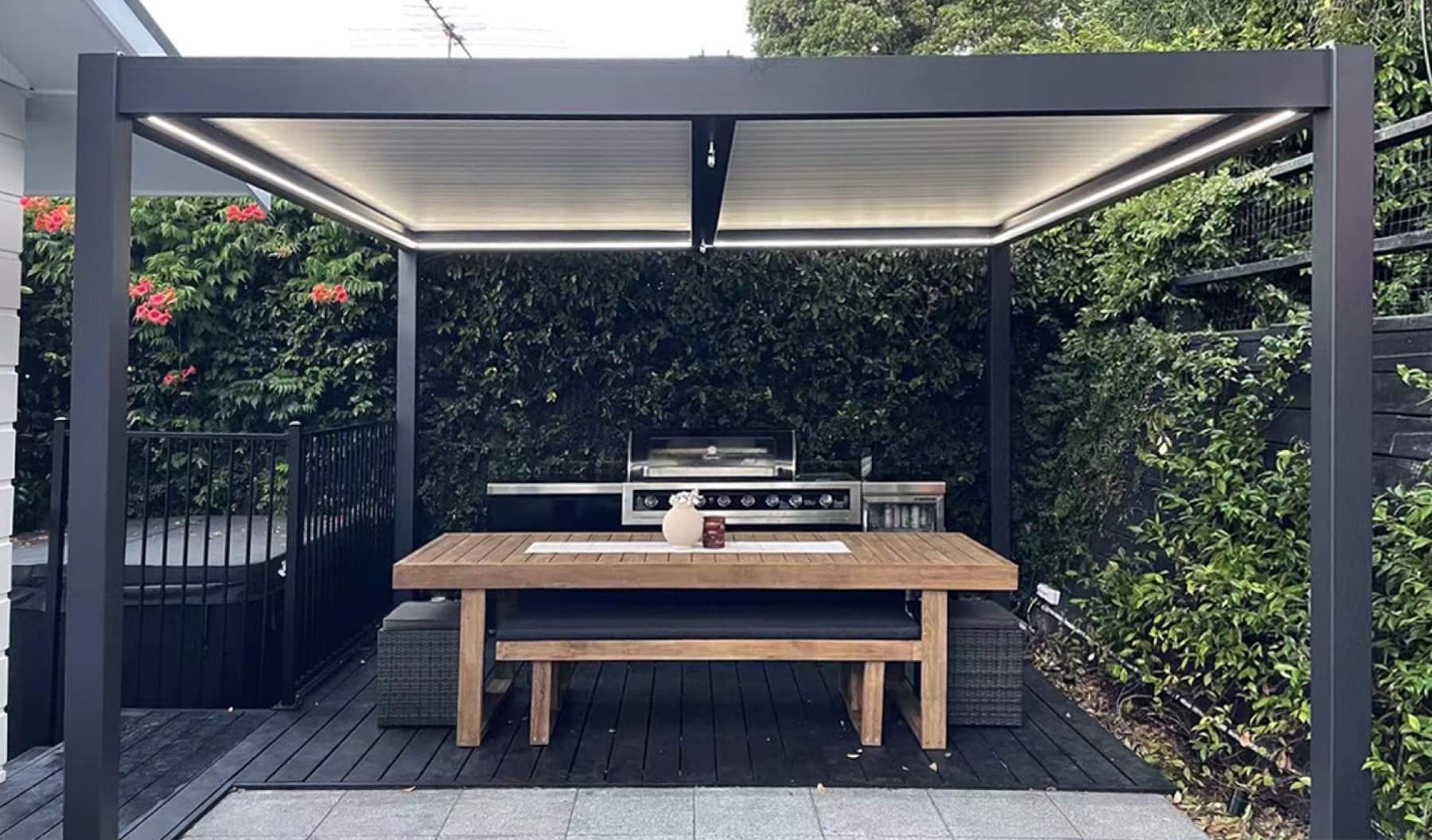 Pergola med integrerat utekök och långbord på en trädäck